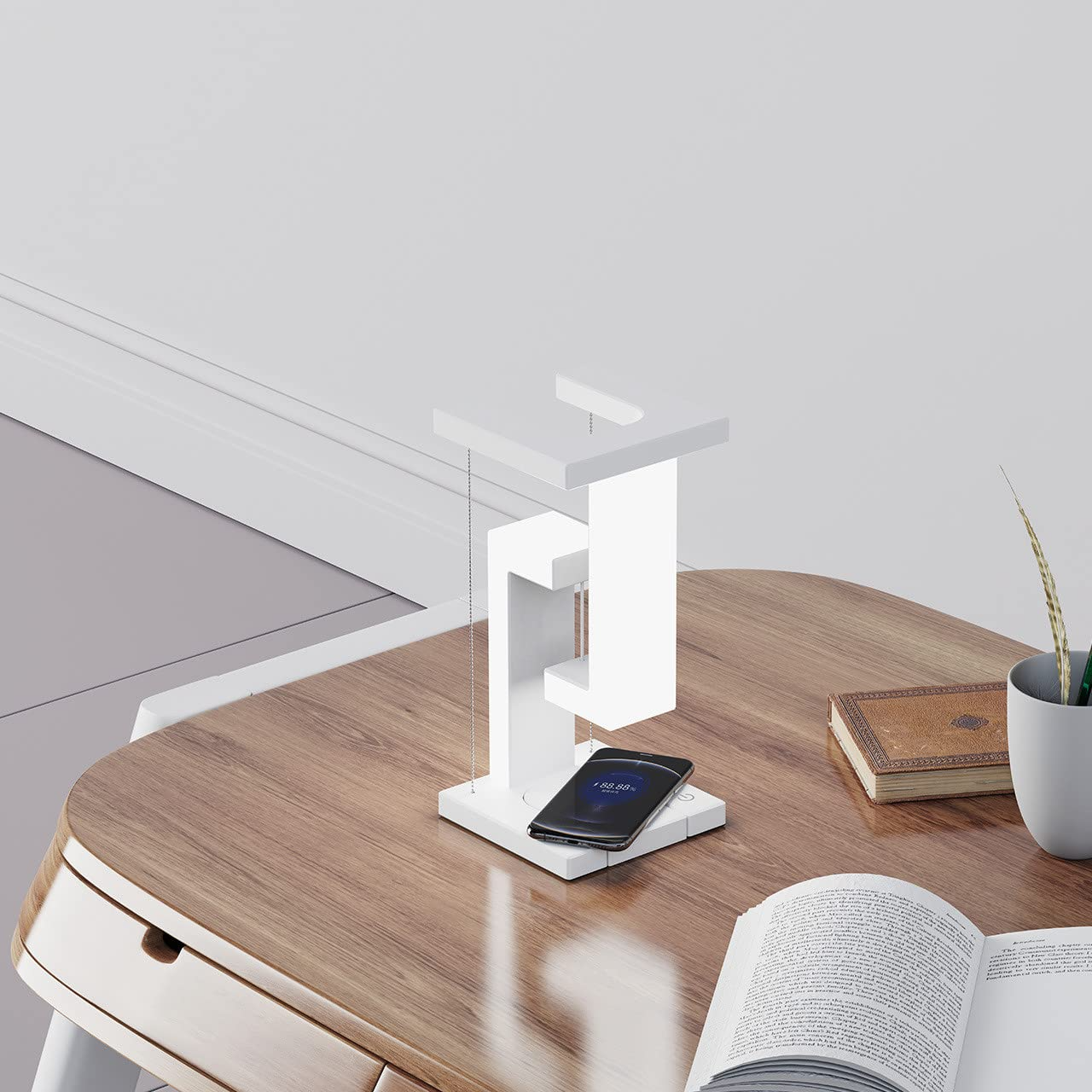 Modern desk setup with a white lamp, smartphone, and open book on a wooden surface.