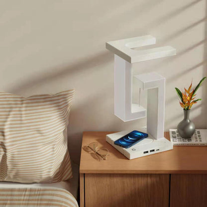 White LED desk lamp on a wooden nightstand with a laptop and other items, next to a bed.