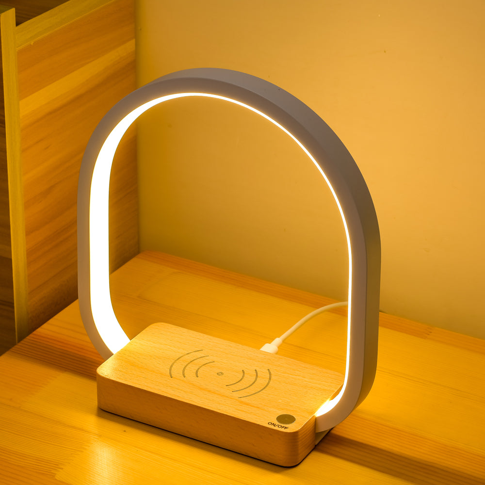 Modern lamp with wooden base and wireless charging pad on a wooden surface.