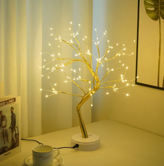 Decorative LED tree on a table with a cup and saucer in a softly lit room.