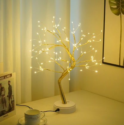 Decorative LED tree on a table with a cup and saucer in a softly lit room.